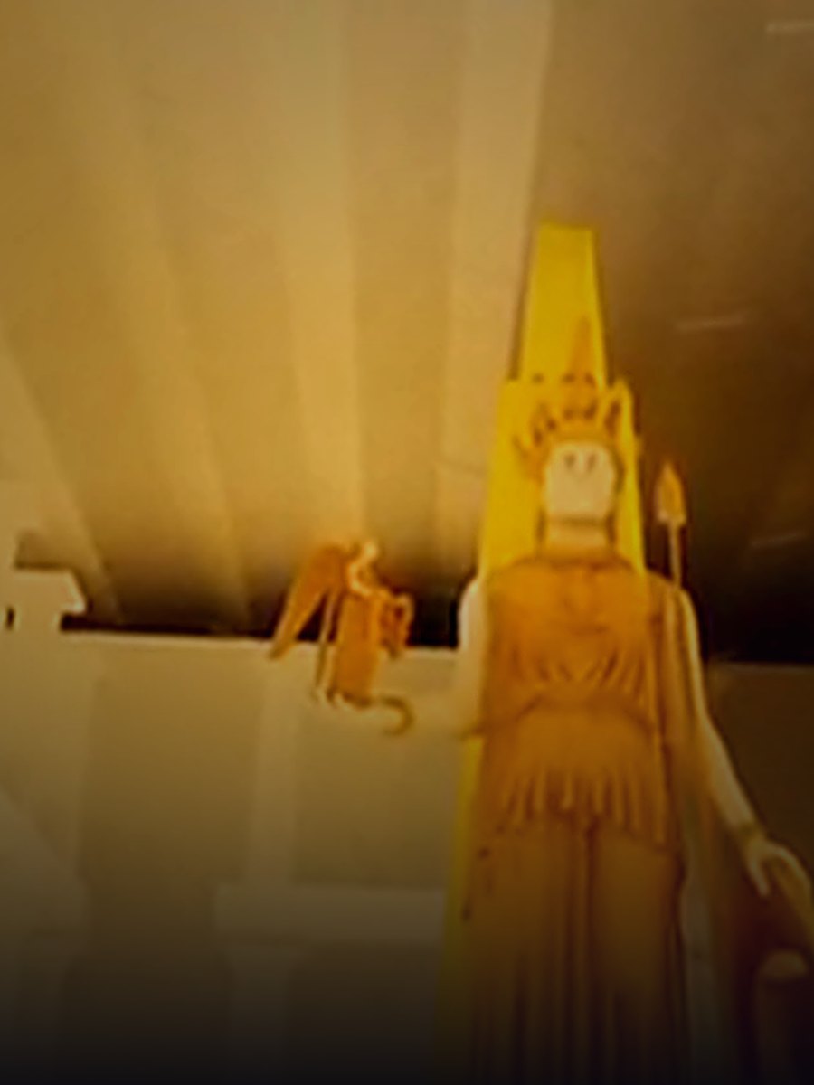 In-engine capture: the Athena Parthenos standing in gold inside the cella, Nike perched on her outstretched hand, the hall lit warm by braziers.